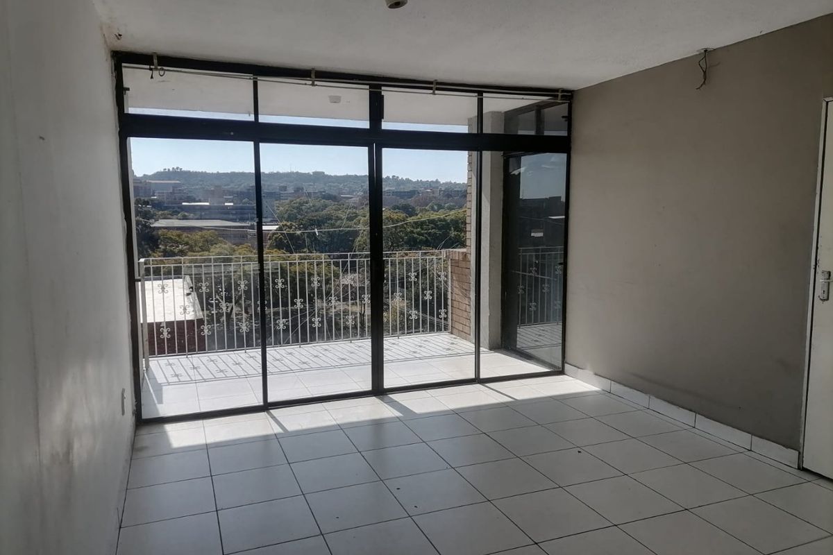 An empty living room featuring tiled flooring and large sliding glass doors that open onto a balcony with an urban view.