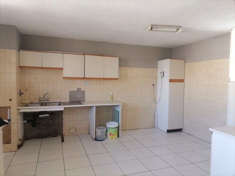 A dated kitchen featuring tiled walls and flooring, built-in cabinetry, and a double sink, currently in need of renovation and modernization.