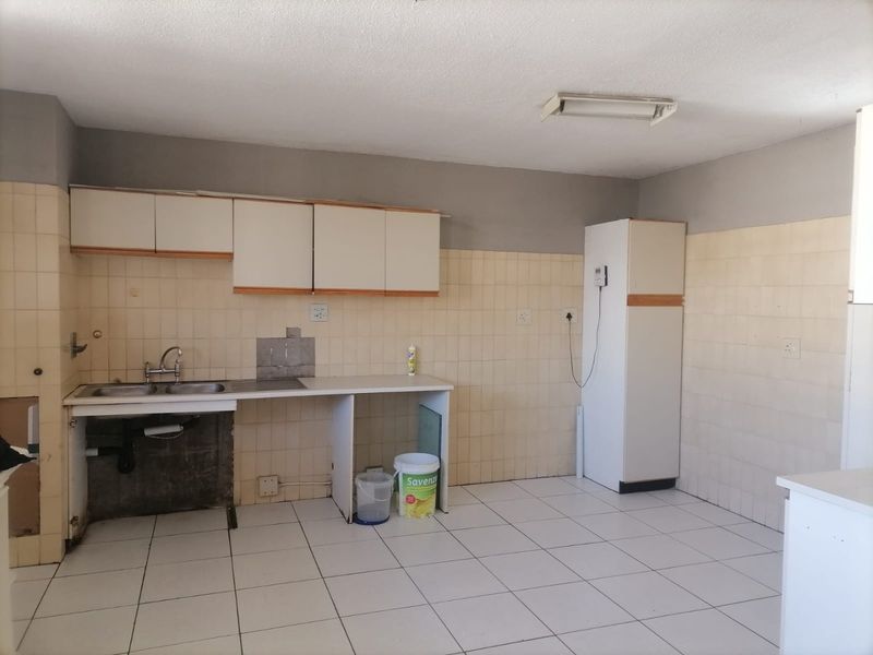 A dated kitchen featuring tiled walls and flooring, built-in cabinetry, and a stainless steel sink, currently in need of renovation and cosmetic updates.