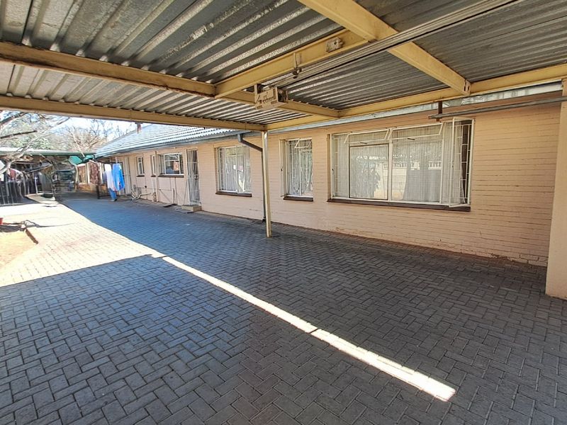 A covered paved outdoor area featuring a corrugated metal roof structure and brick exterior walls, suitable for parking or utility use.
