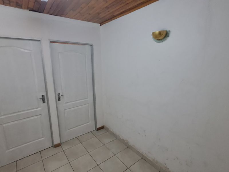 A vacant hallway featuring tiled flooring, a timber ceiling, and two interior doors, showing signs of wear on the walls and floor.