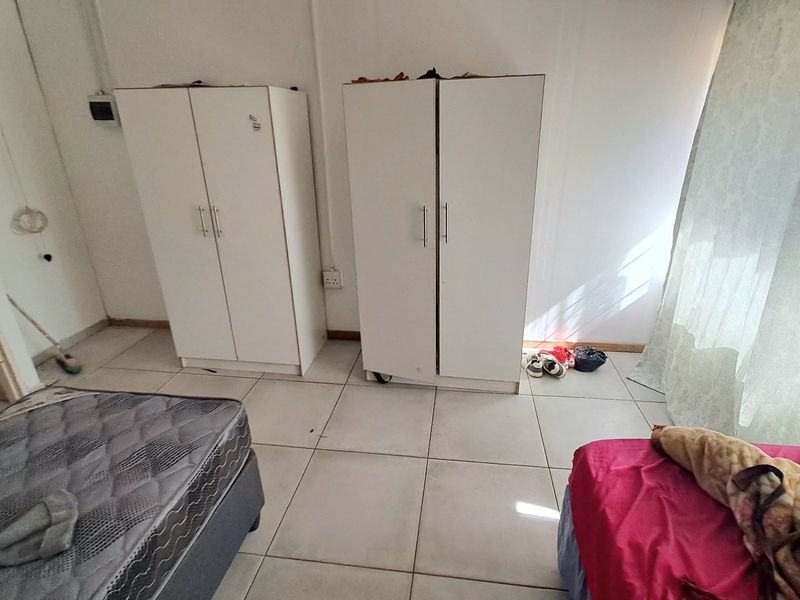 A bedroom featuring tiled flooring and white walls, currently furnished with basic storage units and bedding.