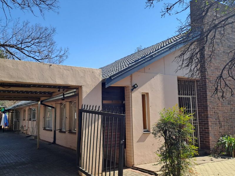 Front exterior view of the house featuring a carport, brick chimney, and paved driveway with security gates and bars.