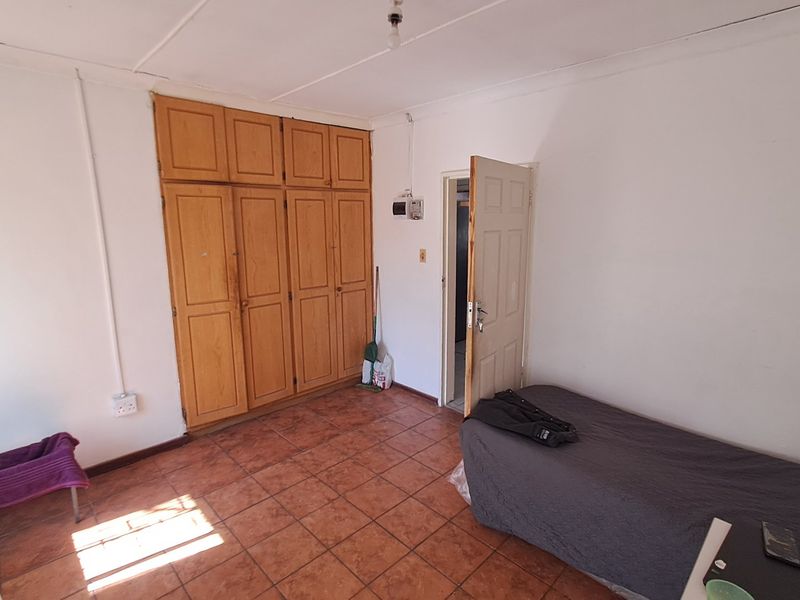 A bedroom featuring built-in wooden cupboards and tiled flooring, offering a functional space with potential for cosmetic updates.