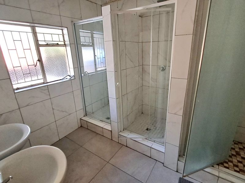 A functional bathroom featuring a double vanity and multiple shower enclosures with tiled finishes, requiring some maintenance and cosmetic updates.