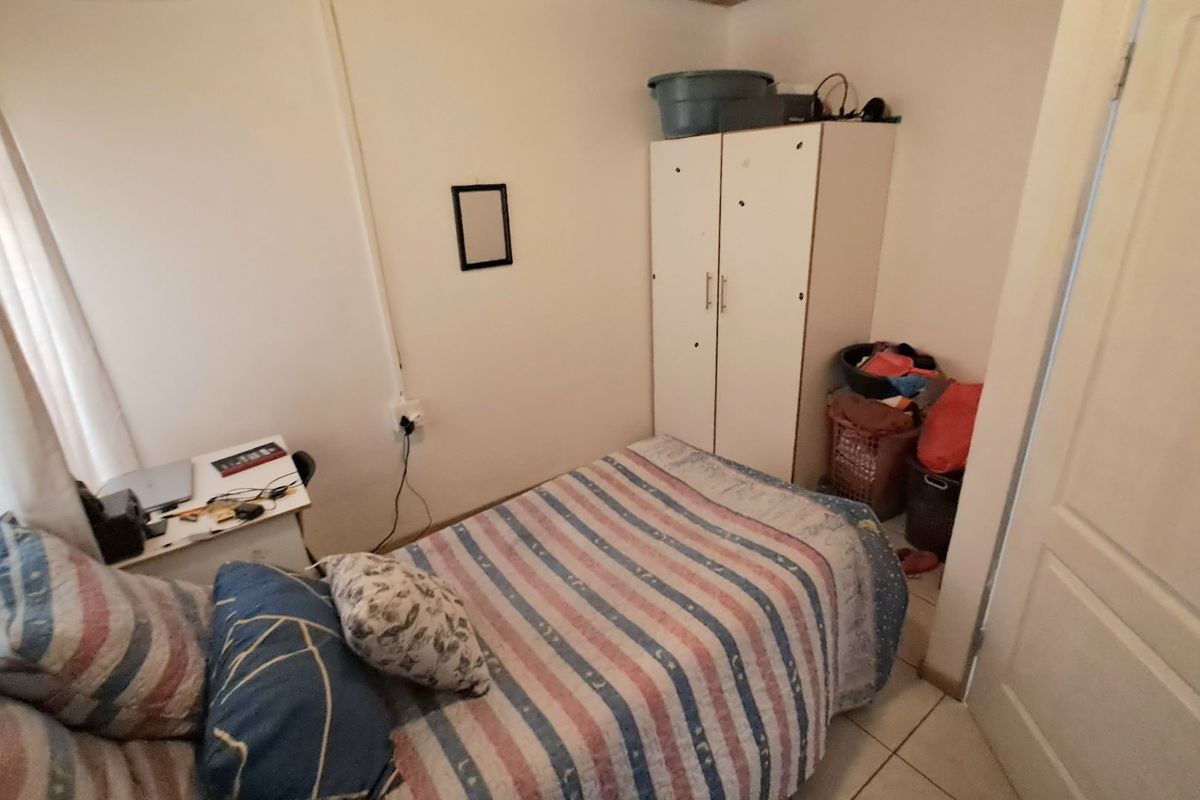 A compact bedroom featuring tiled flooring and a built-in wardrobe, offering a functional space with neutral wall finishes.