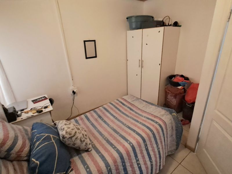 A compact bedroom featuring tiled flooring and a built-in wardrobe, offering a functional space with neutral wall finishes.