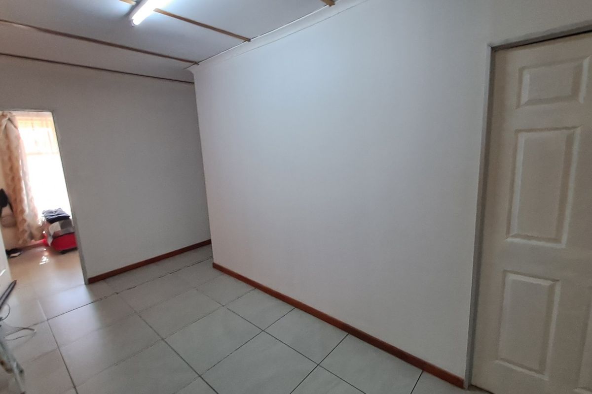An empty living area featuring tiled flooring, white walls, and a panelled interior door, providing a blank canvas for potential interior design updates.
