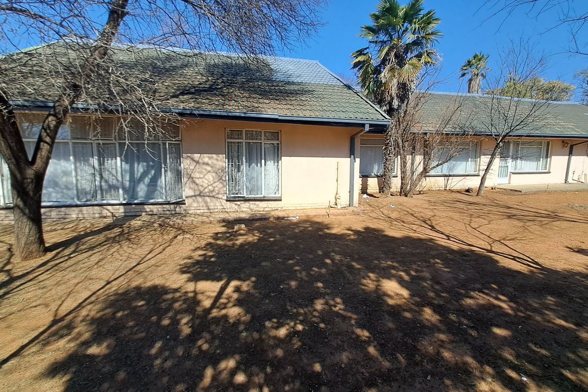 Rear view of a single-story house featuring a tiled roof, large windows with security bars, and a spacious, dry garden area.