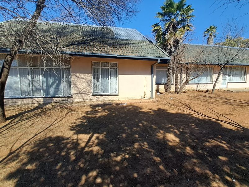 Rear view of a single-story house featuring a tiled roof, large windows with security bars, and a spacious, dry garden area.