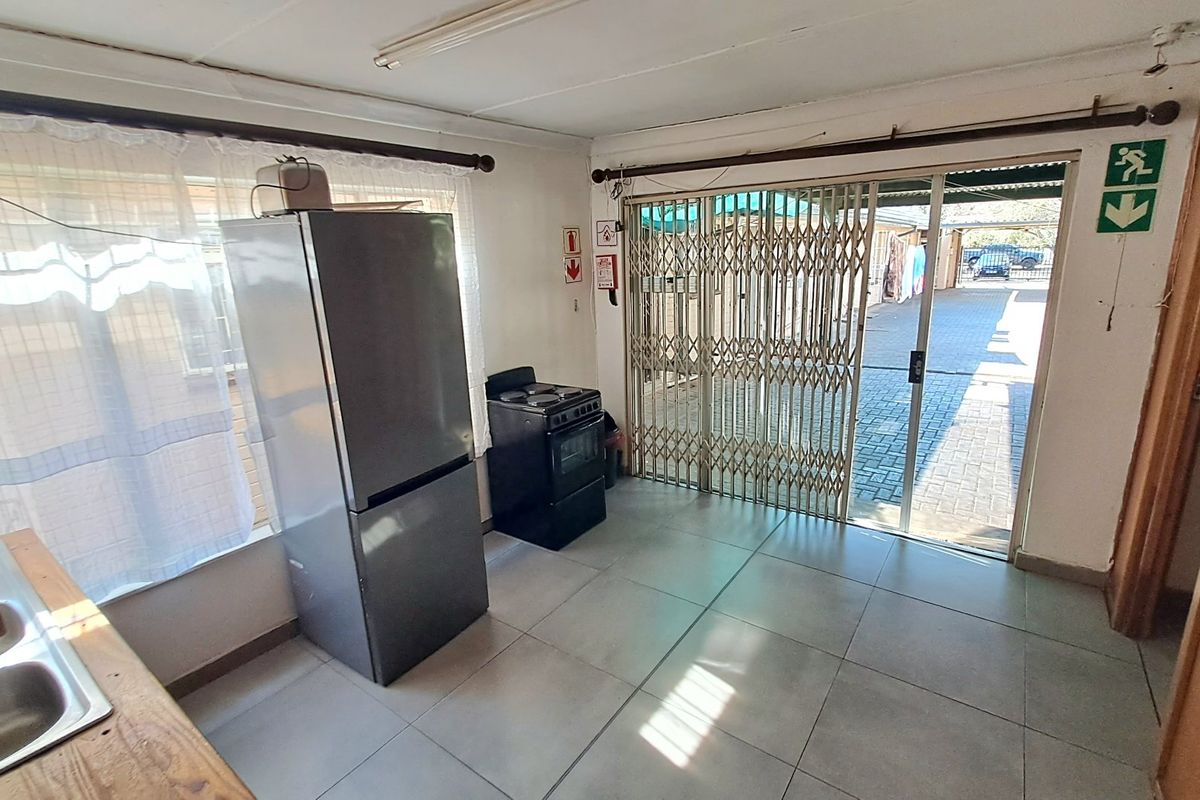 A functional kitchen area featuring tiled flooring, a stainless steel sink, and direct access to the exterior through a sliding glass door with security gate.