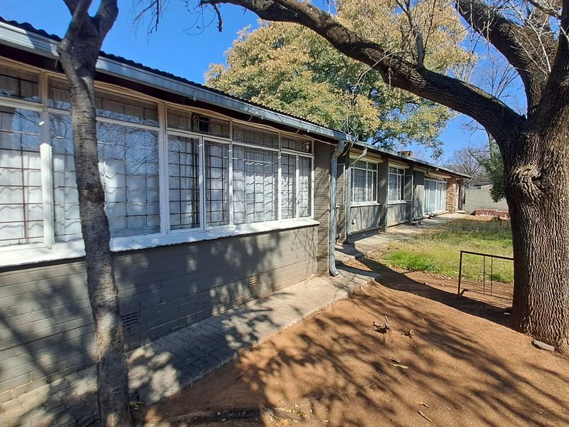 Rear exterior view of the house featuring brick walls, steel-framed windows with security bars, and a paved walkway leading along the building.