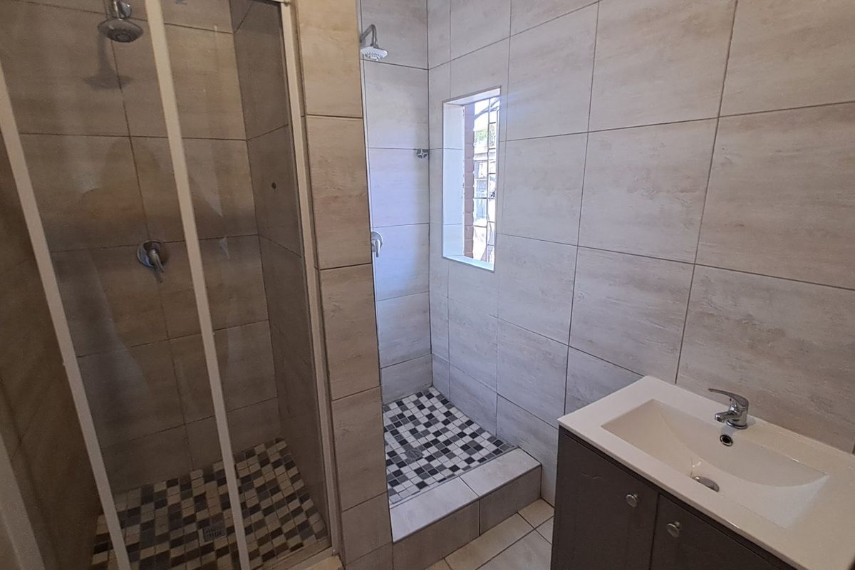 Modern bathroom featuring a glass-enclosed shower, a separate walk-in shower area, and a vanity basin with neutral wall and floor tiling.