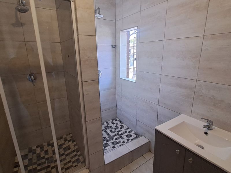 Modern bathroom featuring a glass-enclosed shower, a separate walk-in shower area, and a vanity basin with neutral wall and floor tiling.