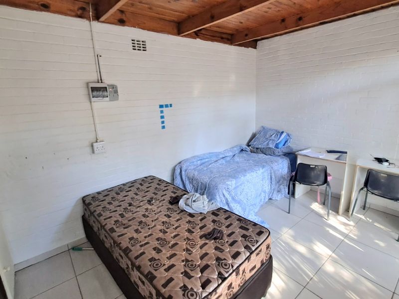 A bedroom featuring exposed timber ceiling beams, painted brick walls, and tiled flooring, requiring cosmetic updates to improve its overall condition.