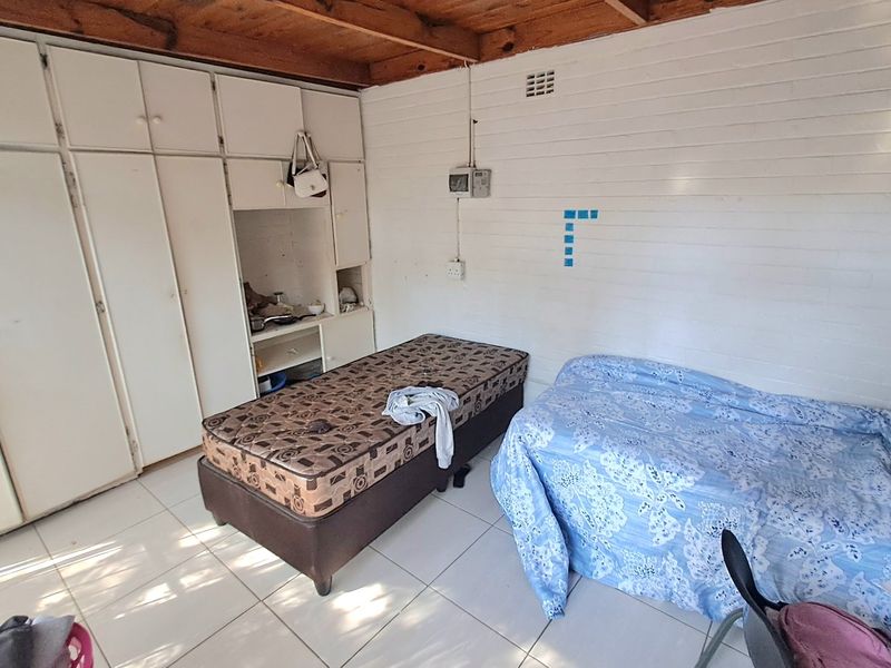 A bedroom featuring built-in cupboards, tiled flooring, and exposed timber ceiling beams, offering a functional space with potential for cosmetic updates.