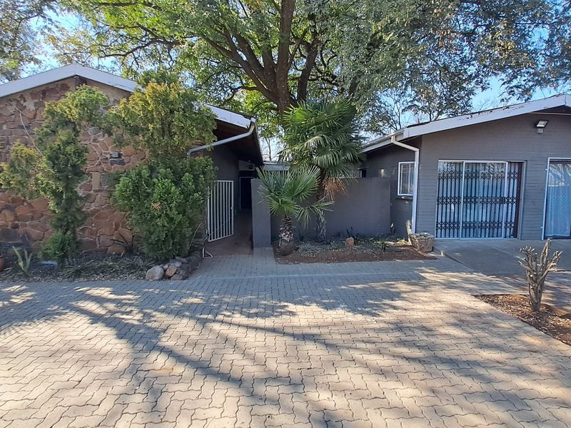 Front exterior view of the property featuring a paved driveway, stone cladding, and secure entrance gates with established garden landscaping.