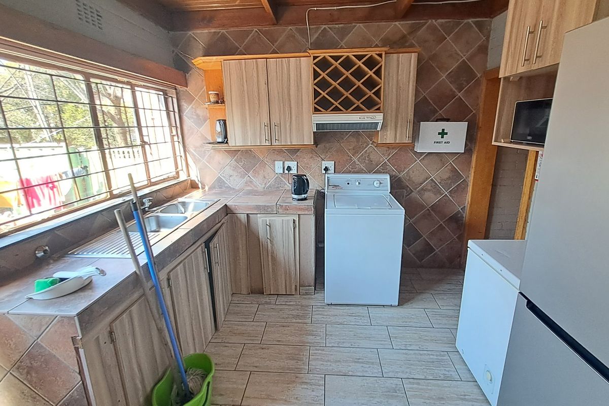 A functional kitchen featuring wood-look cabinetry, tiled backsplash, double basin sink, and exposed timber ceiling beams, offering a practical layout with integrated storage.