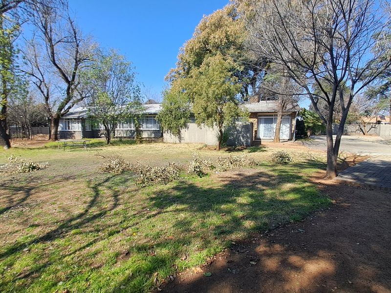 A view of the rear exterior of the house featuring a large garden, mature trees, and a paved driveway area.