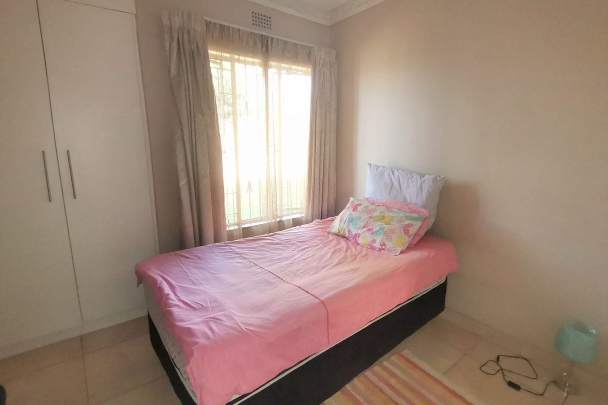 A functional bedroom featuring tiled flooring, a built-in wardrobe, and a window fitted with security bars.