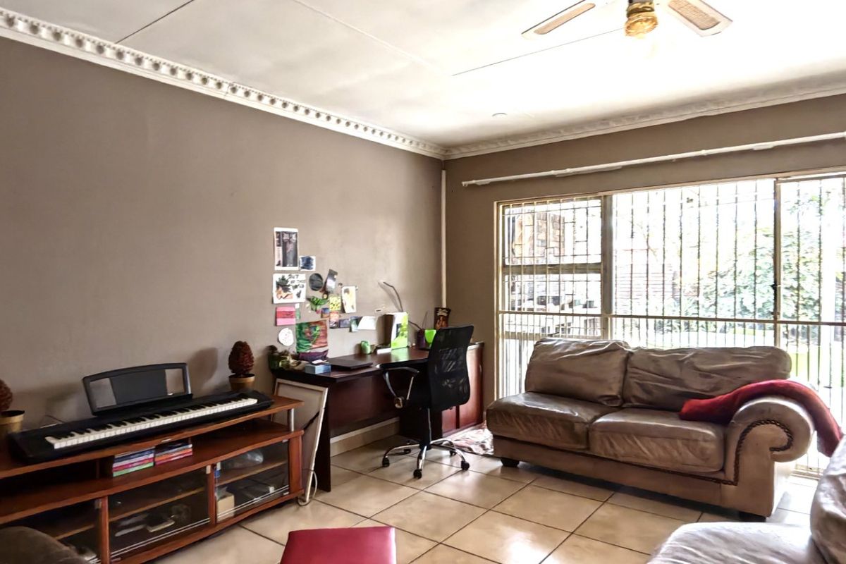 A living room featuring tiled flooring, decorative ceiling cornices, a ceiling fan, and a sliding glass door with security bars leading to the exterior.