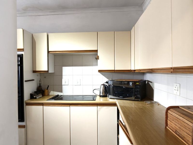 A dated kitchen featuring laminate countertops, built-in cabinetry, and an electric hob, showing signs of wear and ceiling water damage.