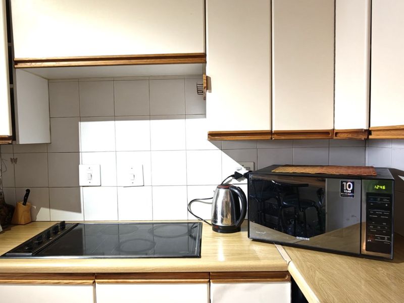 A functional kitchen area featuring laminate countertops, a ceramic tile backsplash, and built-in cabinetry with an integrated electric hob.