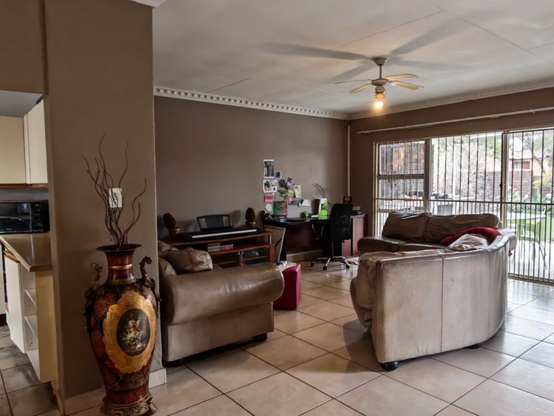 Open-plan living area featuring tiled floors, a ceiling fan, and an adjoining kitchen with built-in cabinetry, leading to a secure outdoor patio area.