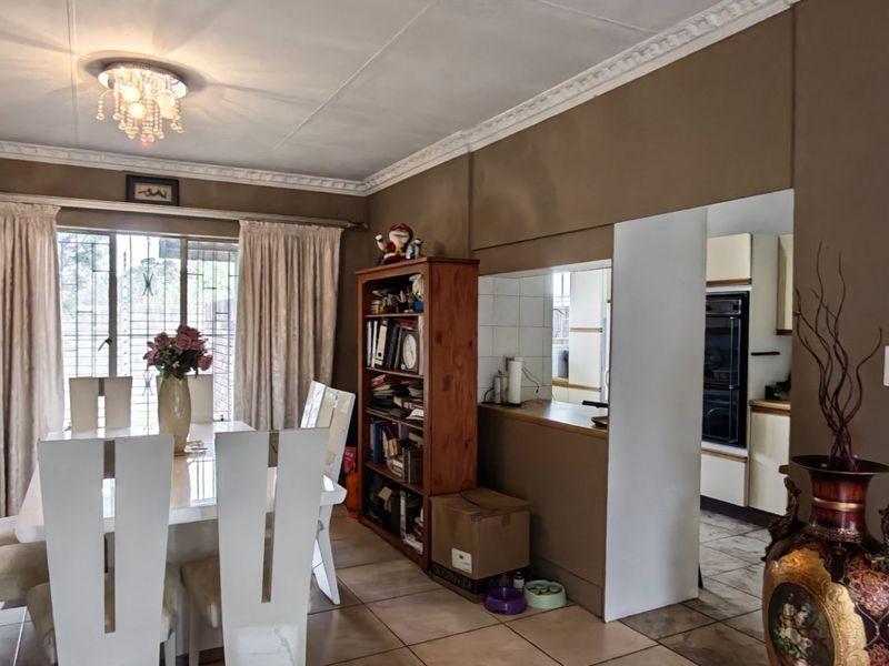 Open plan dining area featuring tiled floors and decorative ceiling cornices, with a pass-through window connecting to the adjacent kitchen.