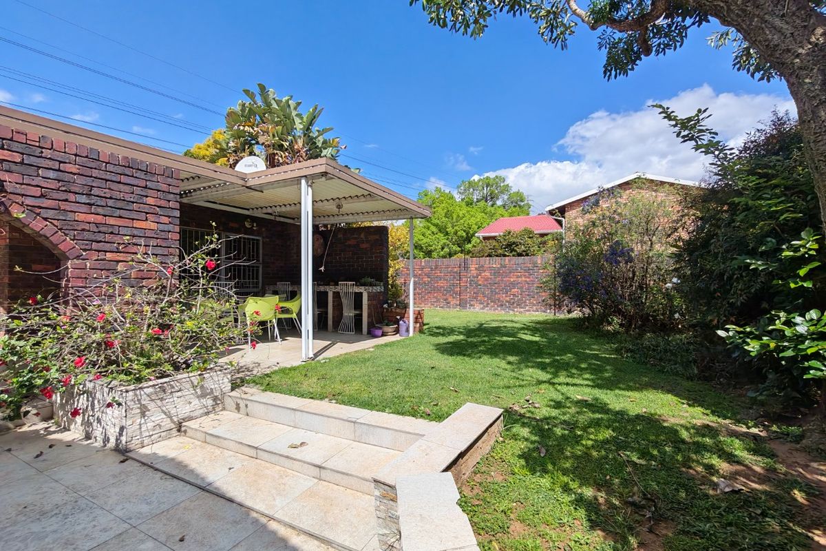 A private rear garden featuring a covered patio area, brick boundary walls, stone-tiled steps, and a well-maintained lawn.