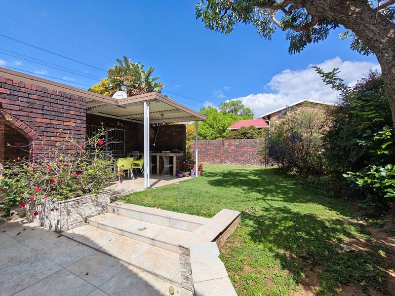 A private rear garden featuring a covered patio area, brick boundary walls, stone-tiled steps, and a well-maintained lawn.