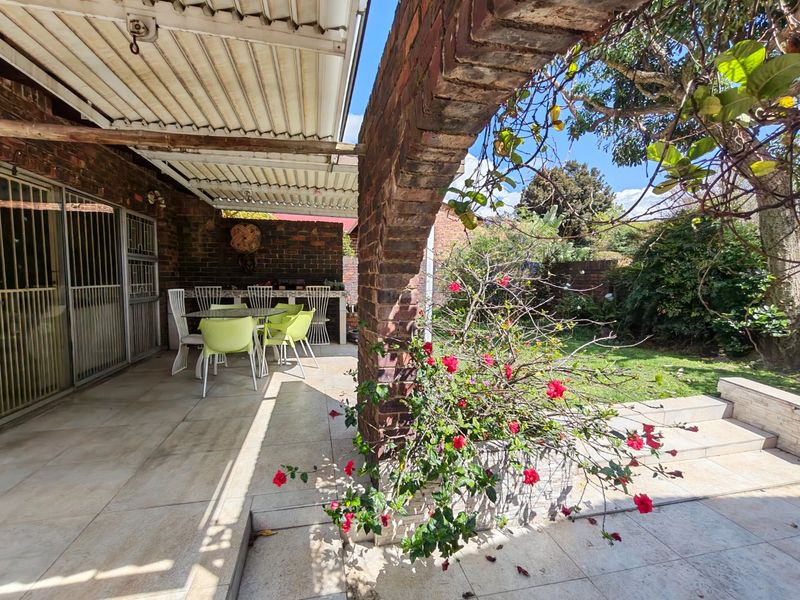 Covered outdoor patio featuring a brick archway, tiled flooring, and a built-in brick counter, overlooking a private garden area.
