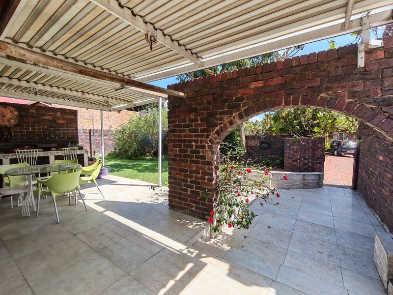 Covered outdoor patio featuring a brick archway, tiled flooring, and a built-in braai area, overlooking a private garden space.