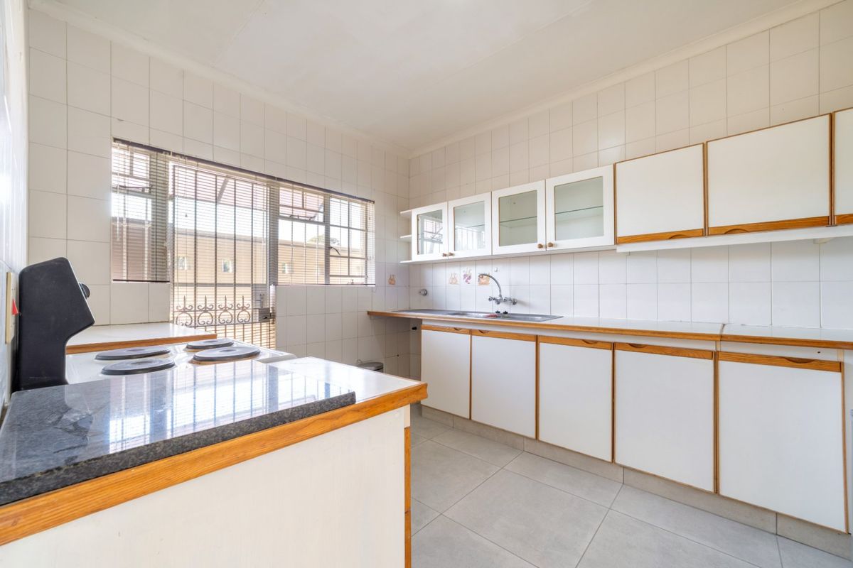 A functional, empty kitchen featuring white cabinetry, laminate countertops, a stainless steel sink, and tiled finishes, ready for modernization.