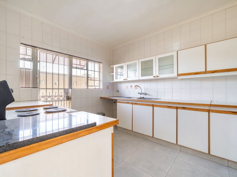 A functional, empty kitchen featuring white cabinetry, laminate countertops, a stainless steel sink, and tiled finishes, ready for modernization.
