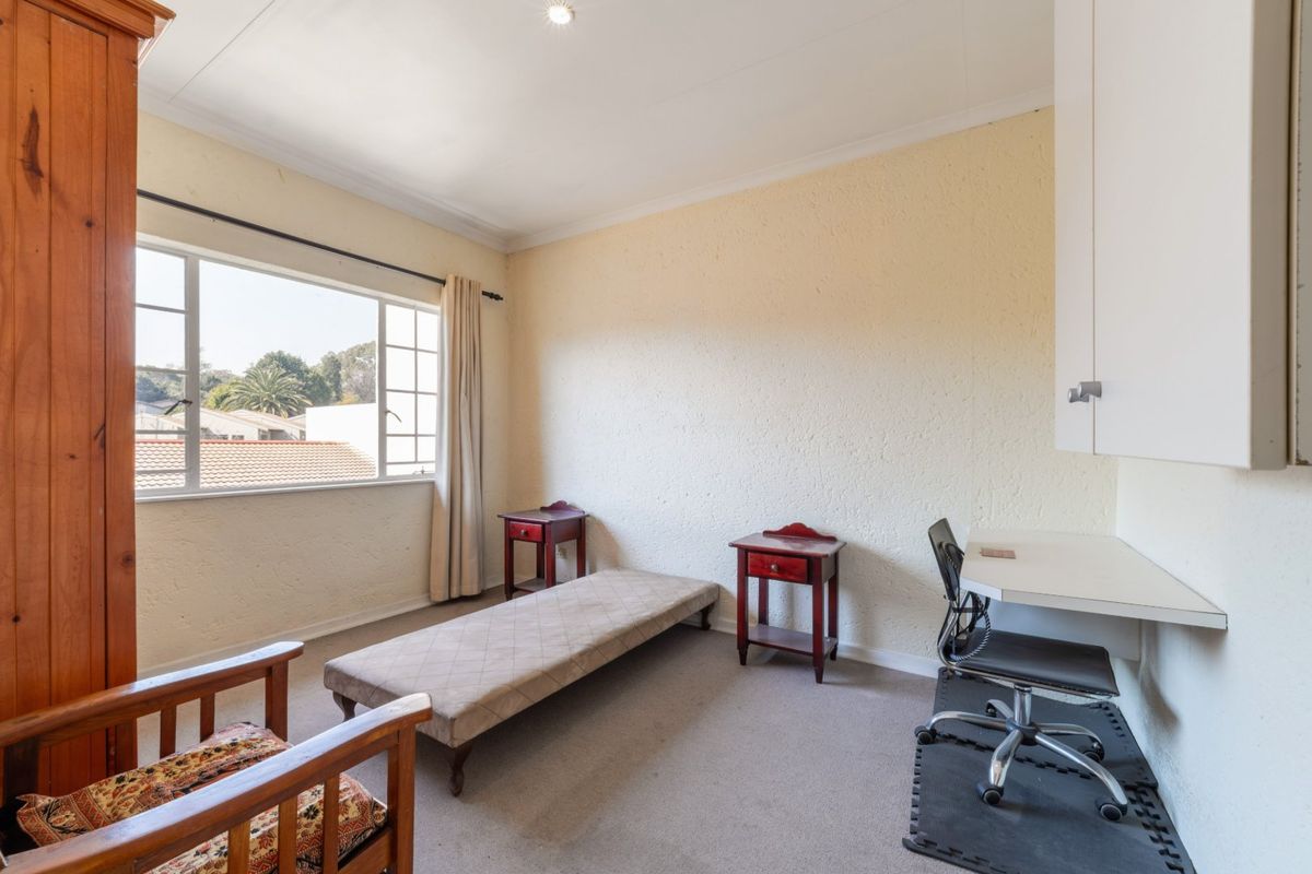 A bedroom featuring a built-in desk, storage cupboard, and large casement window, offering a functional space with potential for modern updates.