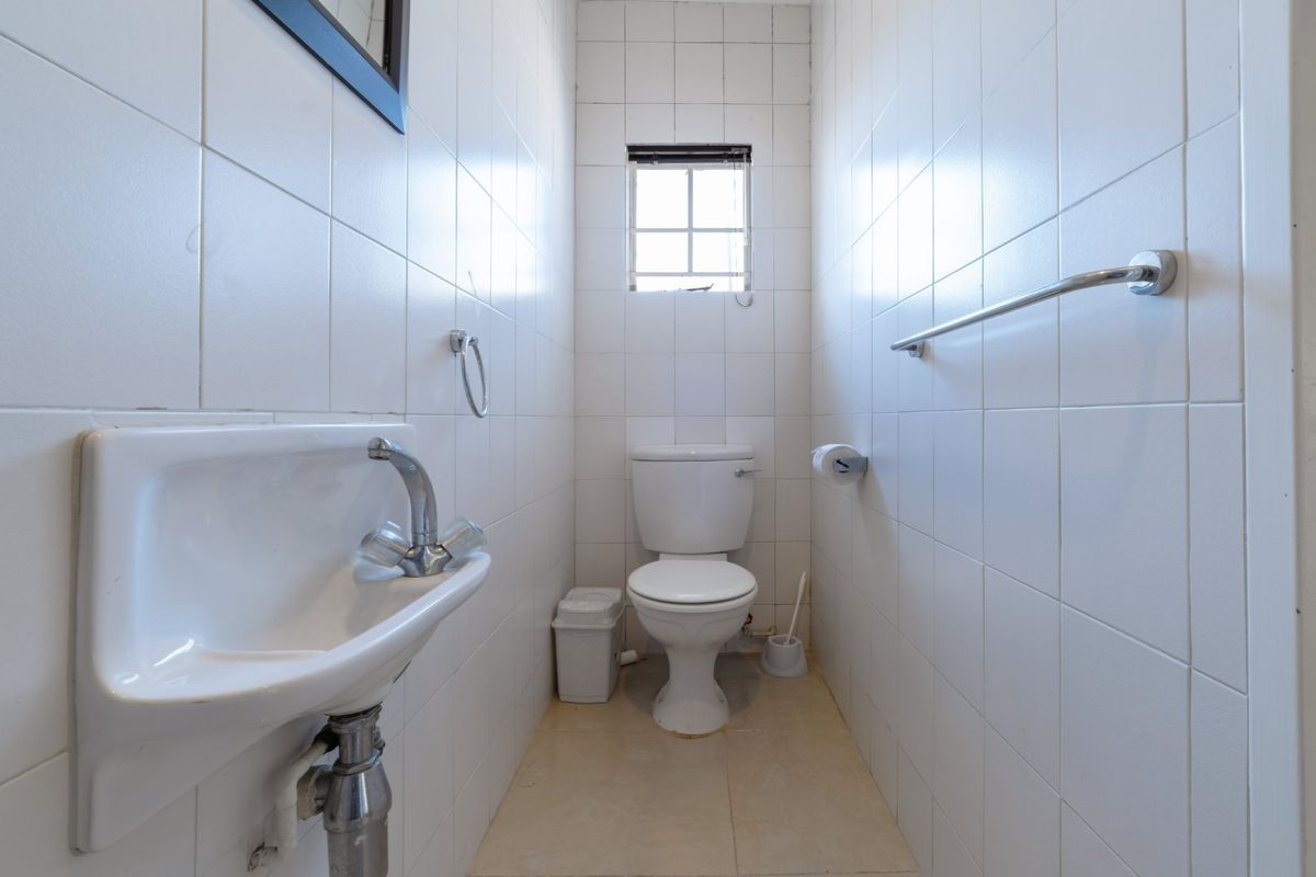 A compact guest bathroom featuring a wall-mounted basin, toilet, and fully tiled walls, requiring some cosmetic updates to improve its overall condition.