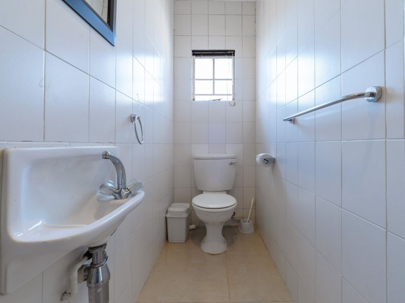 A compact guest bathroom featuring a wall-mounted basin, toilet, and fully tiled walls, requiring some cosmetic updates to improve its overall condition.