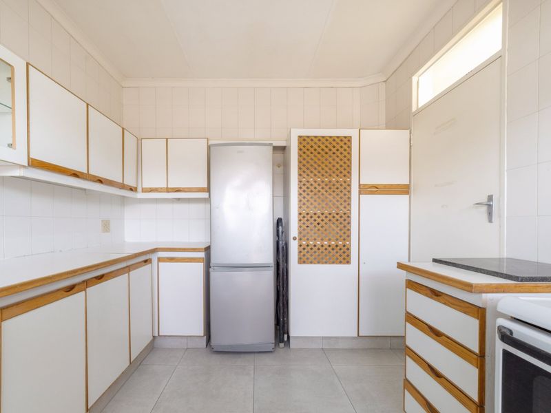 A functional kitchen featuring white cabinetry with wood trim, tiled splashbacks, tiled flooring, and built-in cooking appliances.