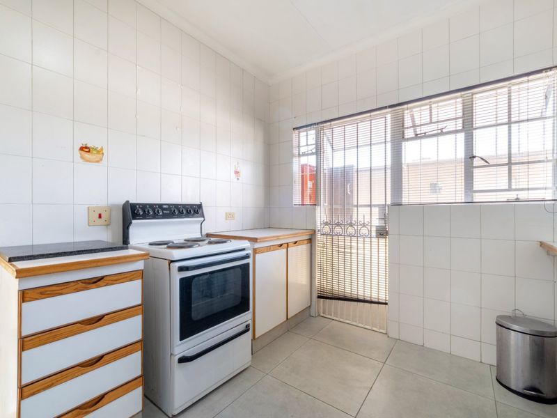 A functional kitchen featuring tiled walls and flooring, built-in cabinetry, and a freestanding stove, with direct access to an exterior security gate.