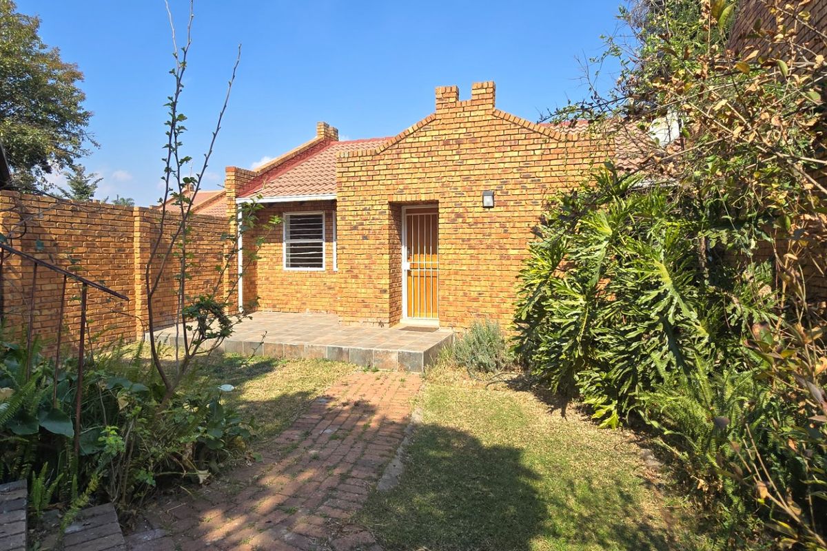 A rear view of a face brick apartment featuring a small tiled patio, brick pathway, and enclosed garden area.