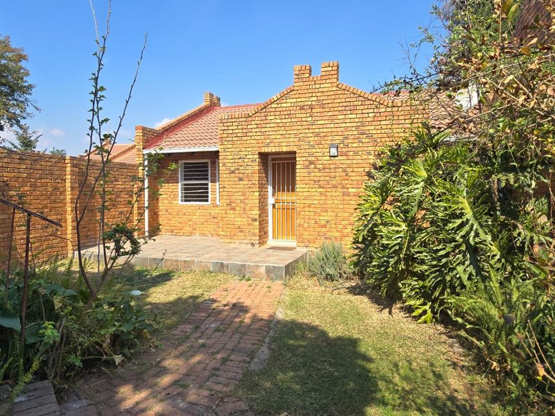 A rear view of a face brick apartment featuring a small tiled patio, brick pathway, and enclosed garden area.