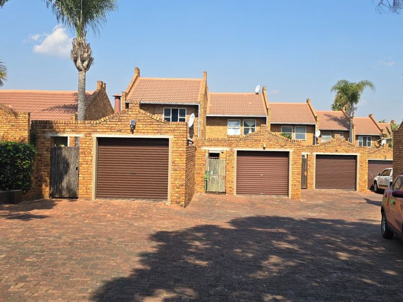 A view of the front facade of a residential apartment complex featuring face brick construction, tiled roofs, and multiple private garages with a paved driveway.