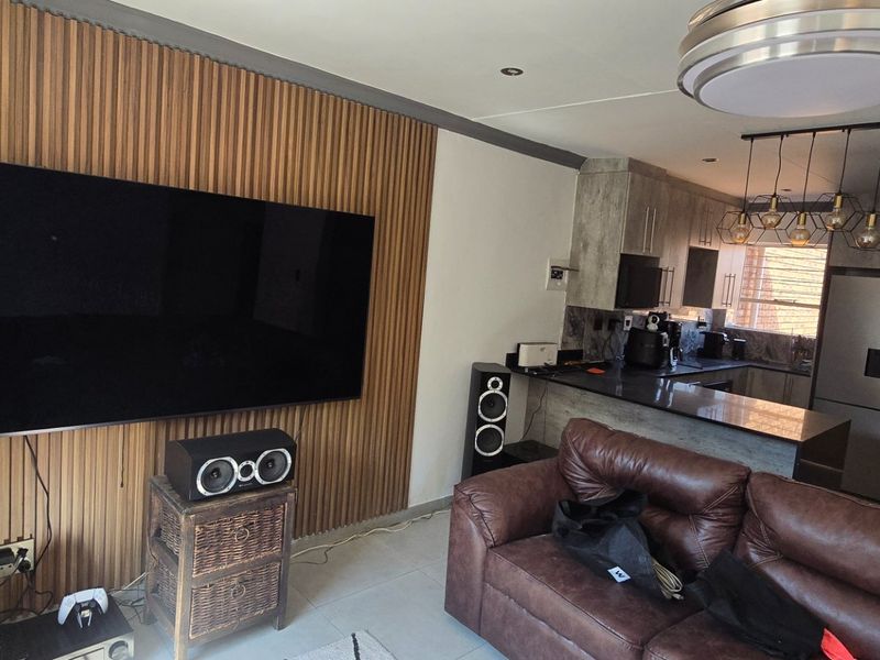 Open-plan living area featuring a modern slatted wood feature wall, integrated kitchen with granite countertops, and contemporary lighting fixtures.