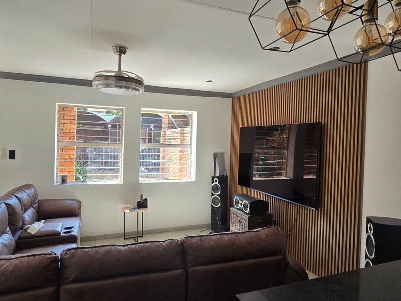 A well-maintained living room featuring a stylish timber slat feature wall, modern pendant lighting, ceiling fan, and tiled flooring with secure window bars.