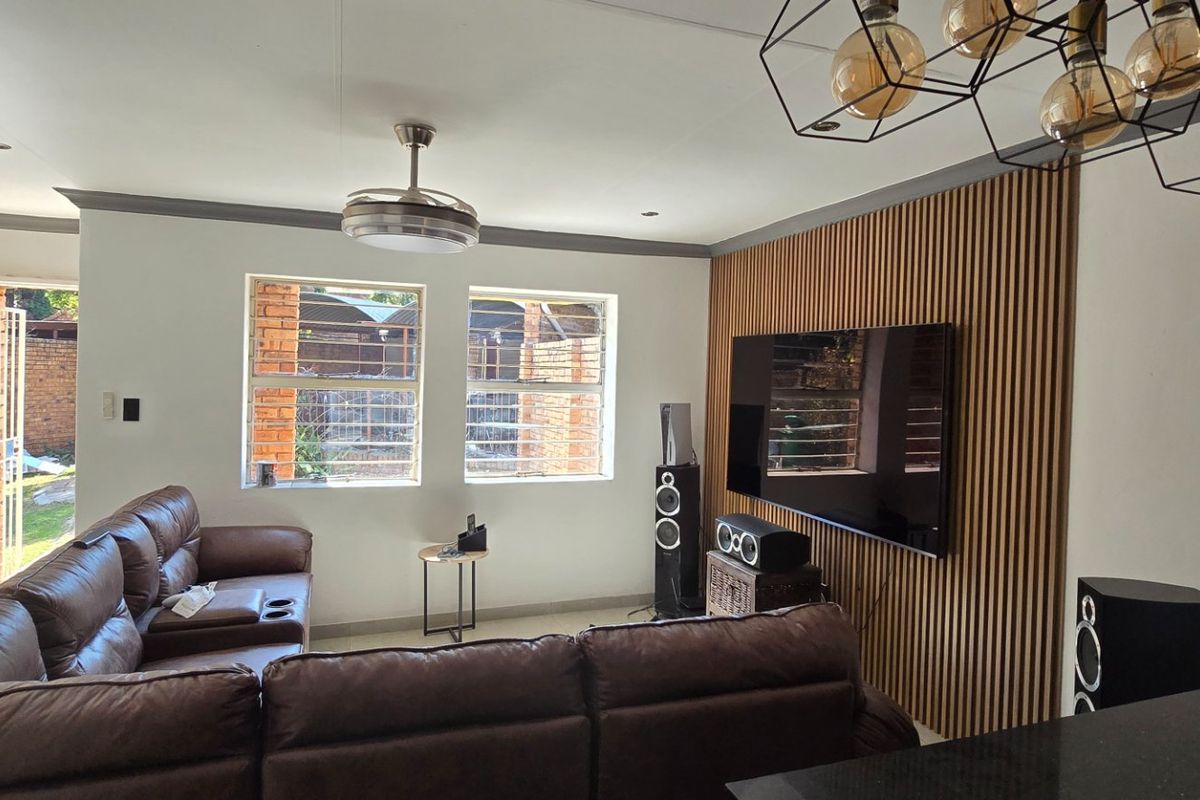A well-maintained living room featuring a contemporary timber slat feature wall, modern pendant lighting, and a ceiling fan, with security bars on the windows.