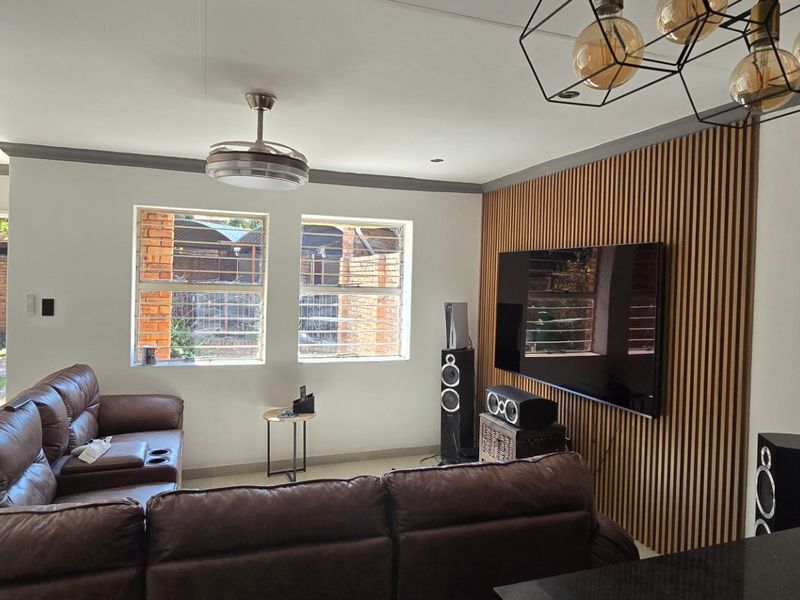 A well-maintained living room featuring a contemporary timber slat feature wall, modern pendant lighting, and a ceiling fan, with security bars on the windows.