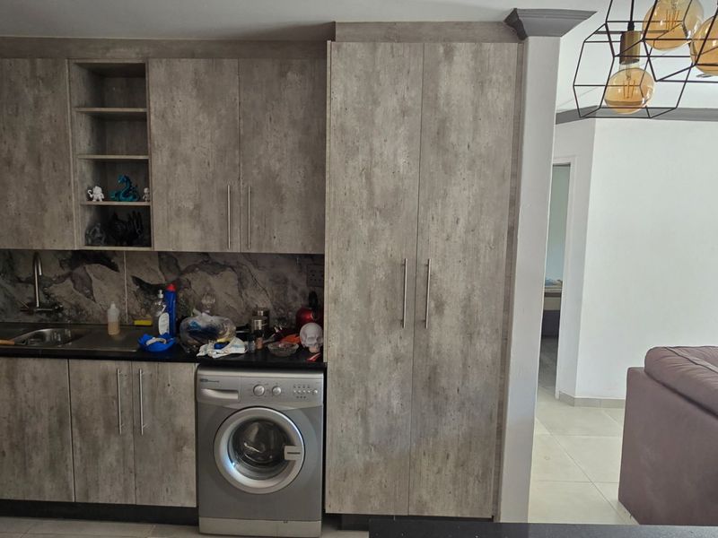 A compact kitchen featuring modern wood-look cabinetry, dark countertops, and an integrated washing machine, seamlessly connected to the adjacent living area.