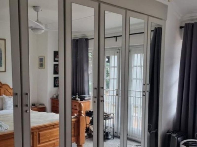 A bedroom featuring a large built-in mirrored wardrobe, a ceiling fan, and access to an outdoor area through glass french doors.