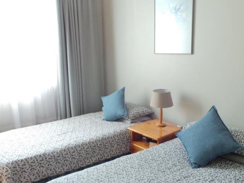 A functional bedroom featuring timber flooring and large windows with curtains, providing a bright and comfortable space.